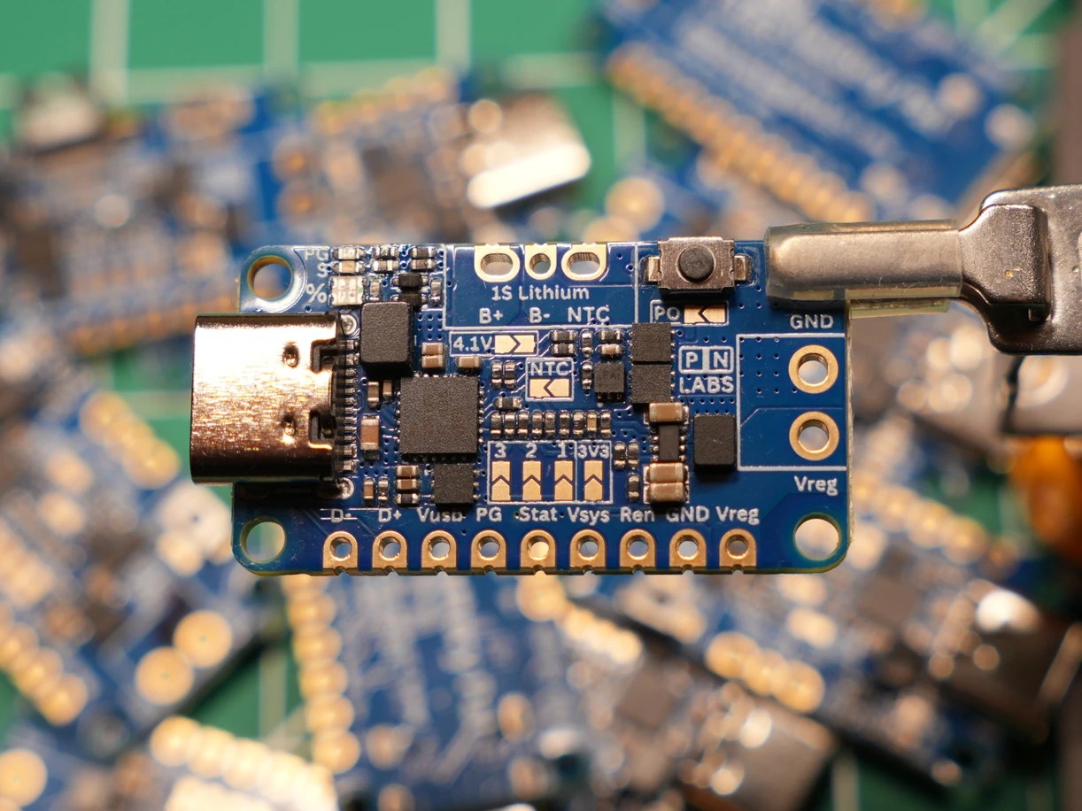 A blue PN Labs power board held above other boards on a workbench
